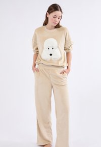 Ensemble loungewear en polaire beige avec un design de chien en peluche blanche sur le sweat-shirt. Coupe ample avec une taille élastique sur le pantalon ; texture douce.