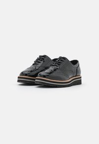 Scarpe in pelle verniciata nera con dettagli brogue, caratterizzate da una punta arrotondata e lacci, elevate da una suola a strati con un accento in legno chiaro.