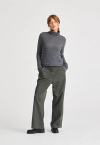 Pulover gri cu guler înalt, asociat cu pantaloni lejeri de culoare verde măsliniu, având un tricotaj texturat și o croială dreaptă, completat cu pantofi negri.