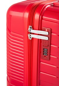 Valigia rigida rossa con superficie testurizzata, doppia cerniera e lucchetto con combinazione integrato, caratterizzata da scanalature verticali per il design.