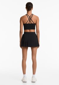 Black sports crop top with crisscross straps; paired with a black pleated skirt. Features a smooth texture and elastic waistband.