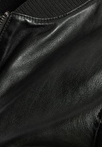 Schwarze Lederjacke mit strukturiertem Finish, mit geripptem Kragen und Reißverschlussdetails. Glattes, weiches Material mit glänzender Optik.