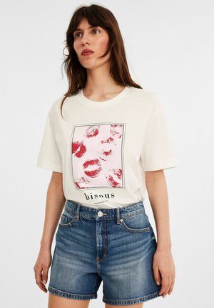 Hvid t-shirt med et rødt kysseprint på et rektangulært design, med ordet "bisous" nederst, parret med denimshorts.