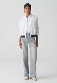 White cropped jacket with black band at hem, paired with light gray wide-leg jeans and white sneakers. The jacket features a button-up front.