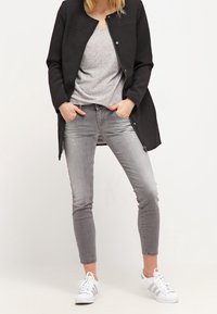 Chaqueta negra, camiseta gris, jeans grises, zapatillas blancas. La chaqueta tiene un corte recto, los jeans son ajustados con un ligero desgaste.