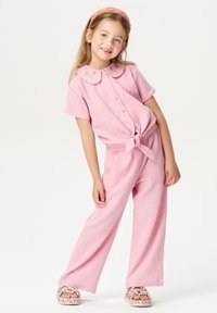 Roze katoenen twee-delig outfit met een collared button-up top met een gestrikt voorpand en wijd-uitlopende broek, gestyled met kleurrijke sandalen.