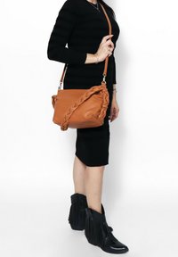 Borsa a tracolla in pelle beige con design intrecciato, dotata di una tracolla. Il materiale sembra liscio con una consistenza morbida. Nessun dettaglio hardware visibile.