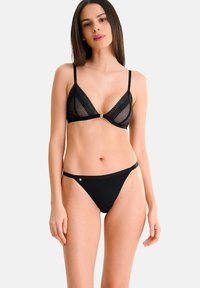 Ensemble de lingerie noire comprenant un soutien-gorge triangulaire avec des panneaux en mesh transparent, des finitions en dentelle et des bretelles ajustables, accompagné d'un string assorti.