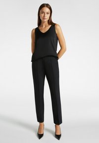 Top nero senza maniche con scollo a V, abbinato a pantaloni neri aderenti con una texture liscia e dettagli discreti nelle cuciture. Tacchi eleganti.