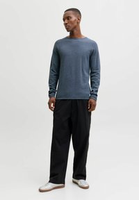 Mørkeblå genser med rund hals og lange ermer, med teksturert finish, kombinert med løse svarte bukser og hvite joggesko med brune detaljer.