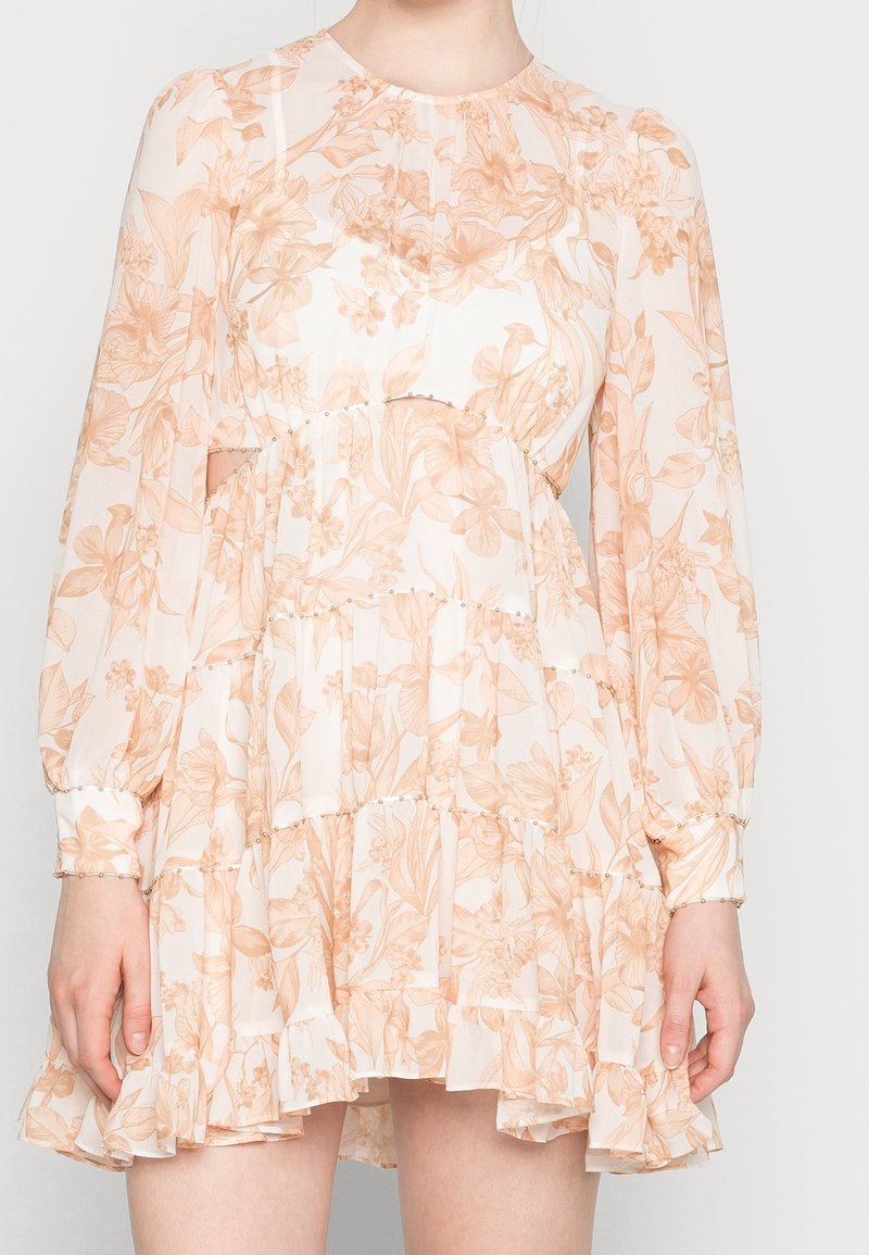 Blommig klänning med en ljus persikofärgad design, lagerpåsar, långa ärmar och subtila pärldekorationer längs midjan och ärmarna.
