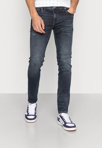 Donkerblauwe skinny jeans met een fitted vorm, voorzien van een vervaagde textuur. Gecombineerd met witte en paarse lage sneakers.