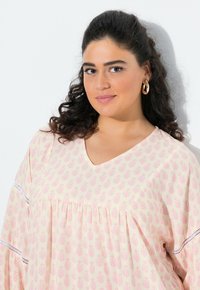 Tunika rosa chiaro con un motivo di foglie, design a V e dettagli arricciati. Rifinita con pizzo sulle maniche.