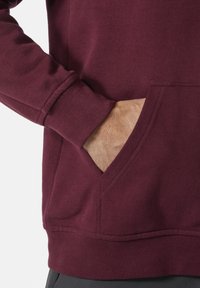 Burgundská mikina z měkké tkaniny s klokaní kapsou a žebrovanými manžetami. Tkanina má hladkou strukturu a minimální švy.