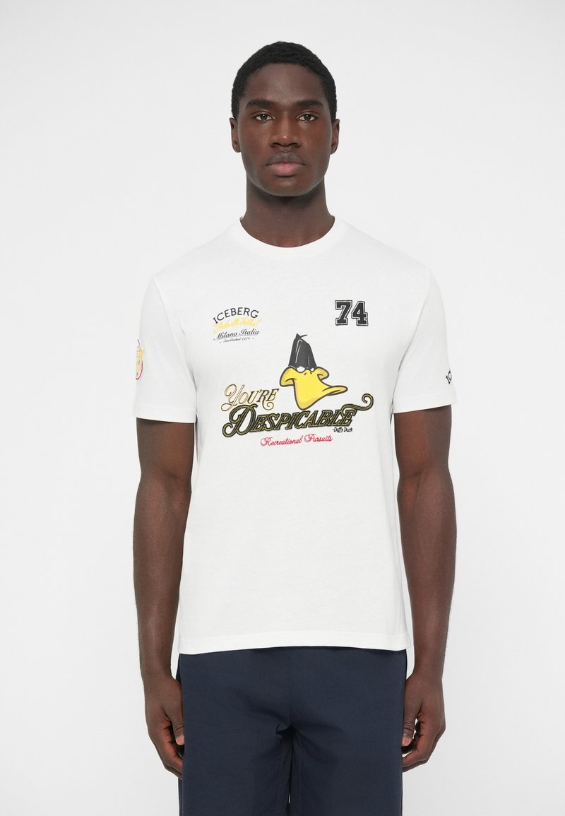 Λευκό βαμβακερό T-shirt με στρογγυλή λαιμόκοψη, τυπωμένα γραφικά με κίτρινο παπάκι και ποικίλα κείμενα σε μαύρο και κόκκινο. Κανονική εφαρμογή.