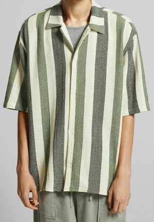 Persoon die een overhemd met korte mouwen draagt met brede verticale strepen in groen, zwart en crème over een grijs T-shirt.