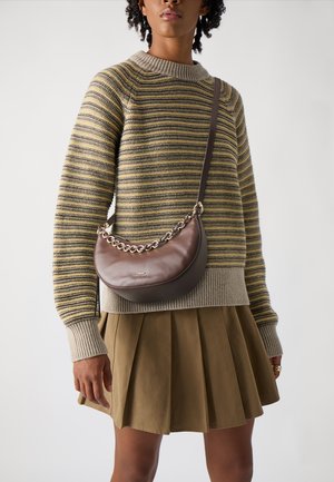 Brun læder crossover taske med en buet form, sølv kæde detalje, båret over en stribet sweater og en plisseret khaki nederdel.