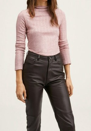Femme portant un haut à manches longues côtelé rose clair rentré dans un pantalon noir en cuir synthétique à taille haute sur un fond uni.