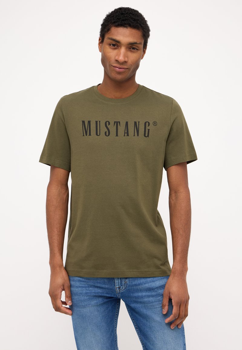 Alavijo žalios spalvos trumpas rankovėmis marškinėliai su apvaliu kaklu, kuriuose priekyje yra juodas užrašas "MUSTANG". Minkšta medvilnė.