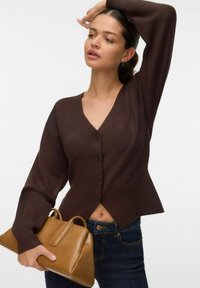 Bruine gebreide cardigan met V-hals, knoopdetails en flared mouwen, gecombineerd met een tan handtas. Draag het met donkerdenim jeans.