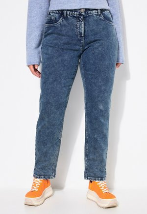 Jeans aus Denim in verblasstem Blau mit geradem Schnitt; ausgestattet mit fünf Taschen und einem Bund; kombiniert mit orangefarbenen Turnschuhen mit weißen Schnürsenkeln.