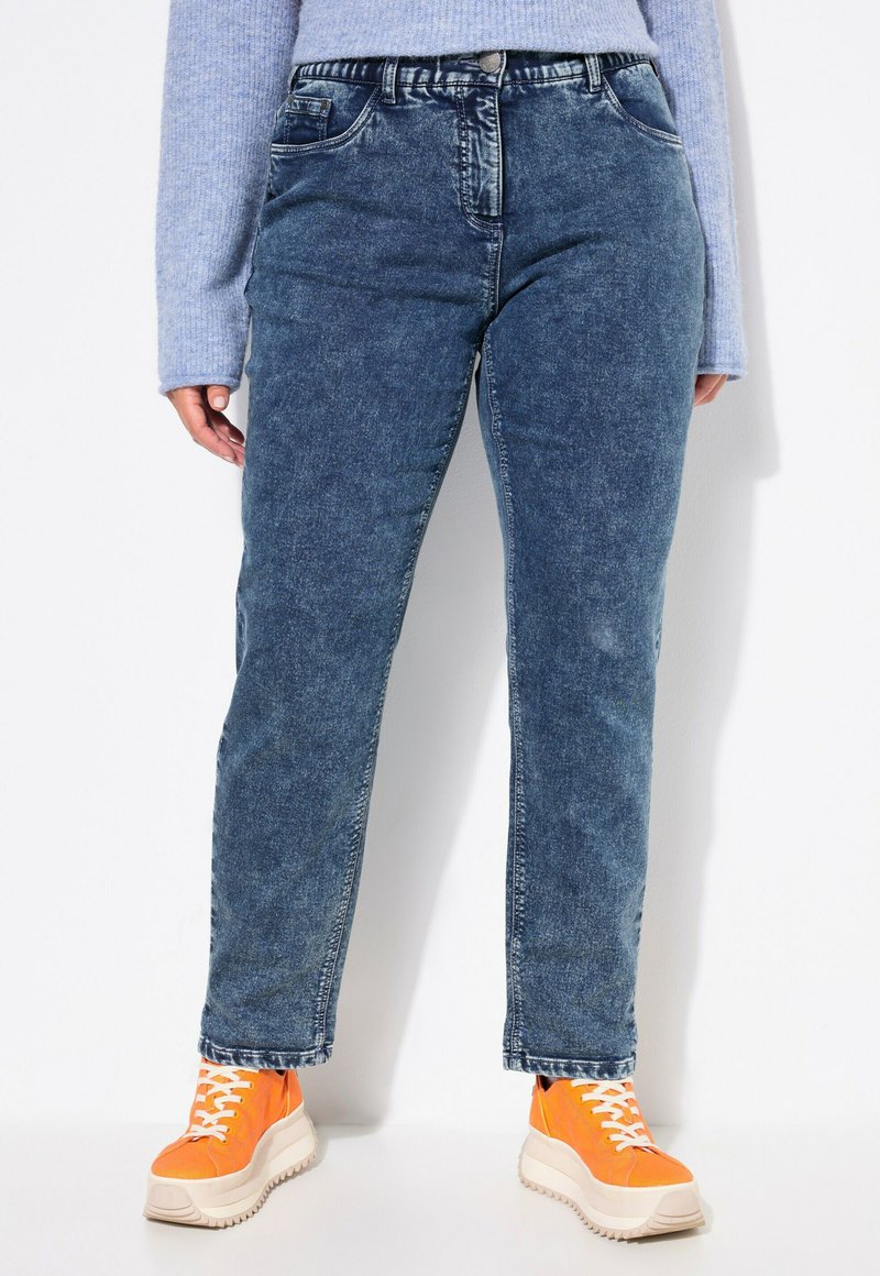 Vaqueros de mezclilla en azul deslavado con corte recto; cuentan con cinco bolsillos y una cinturilla; combinados con zapatillas naranjas con cordones blancos.