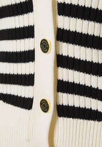 Gestreifter Cardigan in Schwarz und Weiß mit geripptem Struktur, großen goldfarbenen Knöpfen mit Markenlogo und einer durchgängigen Knopfleiste.