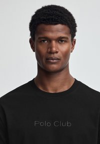 Svart sweatshirt med rund hals och präglad "Polo Club"-logotyp på framsidan. Slät tygstruktur och figurnära design.