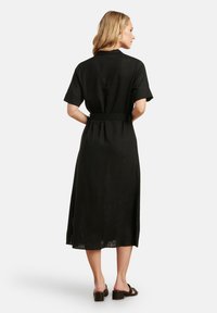 Schwarzes Leinenkleid mit kurzen Ärmeln, taillierter Taille und Länge bis zur Mitte der Waden. Hat ein einfaches Design und einen leicht strukturierten Stoff.