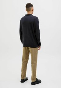 Mørk grå langermet polo skjorte med avslappet passform, kombinert med lyse khaki bukser og svarte joggesko, sett bakfra.