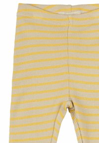 Sárga és krém csíkos leggings, bordás anyagból. Rugalmas derékpánttal rendelkezik, és szűk szabású lábai sima tapintásúak.