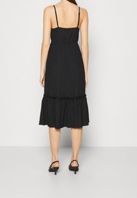Robe midi noire à fines bretelles, taille froncée et ourlet à volants. Confectionnée en tissu texturé, avec un design simple et classique.