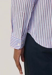 Overhemd met knoopsluiting en verticale strepen in blauw, rood en wit. Opvallende details zijn de afgeronde zoom en de manchetten met witte knopen.