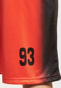 Punaiset ja mustat gradientti urheilushortsit, joissa on sileä pinta ja joissa on sivulla näkyvällä paikalla suuri musta "93" painatus.