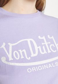 Světle fialové bavlněné tričko s bílým ohraničeným nápisem "Von Dutch ORIGINALS." Kulatý výstřih, měkká textura, krátké rukávy.