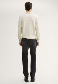 Heledbež žirgepingiga polo särk, mille varrukad on ribadest ning sobitatud tumedate hallide teksade ja mustade kingadega, nähtuna tagant.