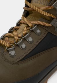 Pruun matkasuss, millel on heledad ja burdeos värvi paelad, metallist silmused ja tekstureeritud mustad aktsendid. Omab pehmet kraed ja kummist tallat.