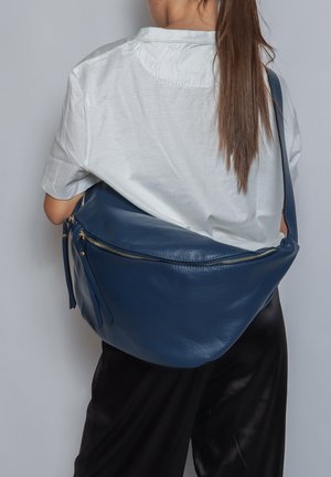 Borsa hobo in pelle blu con una texture liscia, forma curva e dettagli in metallo dorato. Indossata sulla spalla, evidenziando un design pratico.