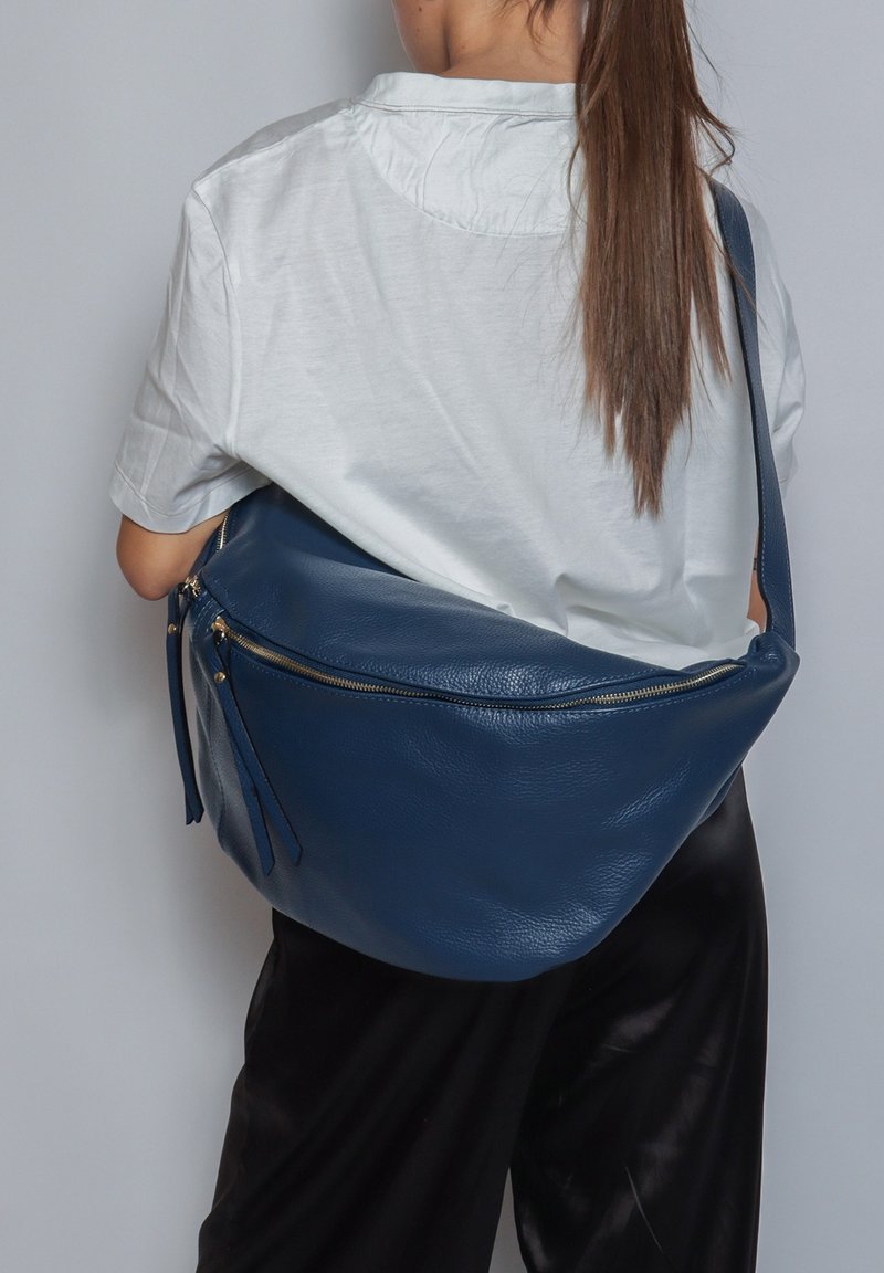 Blauwe leren hobo-tas met een gladde textuur, gebogen vorm en gouden ritsaccenten. Gekozen om over de schouder te dragen, wat een praktische vormgeving laat zien.