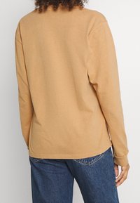 Långärmad T-shirt i ljust brunt bomull, med avslappnad passform, rund halsringning och ribbade ärmslut, kombinerad med blå denimjeans.