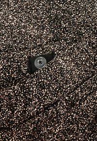 Zwarte stof met een gestructureerd patroon van metallic roségouden stippen; heeft een zwarte stoffen lus met zilveren knoopaccenten.