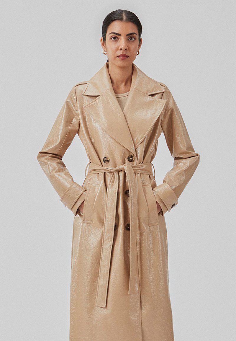 Beige, blank, trenchcoat med dobbeltknap, store revers og talje bælte. Omfatter sidelommer og strukturerede ærmer.