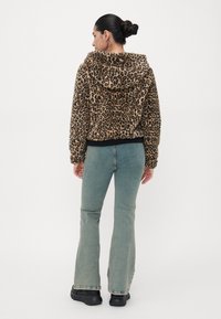 Brun og svart leopardmønstret hettegenser med hette, myk tekstur, ribbet nederkant, kombinert med lyseblå flagrende jeans og svarte sko.