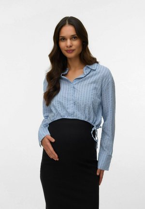 Gravid kvinde med langt mørkt hår, iført en blåstribet bluse og sort nederdel, der blidt holder om sin mave.