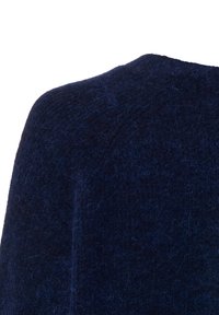 Close-up van een donkerblauwe wollen blazer schouder met zichtbare textuur en subtiele vezels tegen een witte achtergrond.
