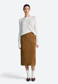 Beli pleteni pulover z dolgimi rokavi, kombiniran z rjavo semiš krilo do sredine tele. Model nosi krem nogavice in rjave koničaste pete.