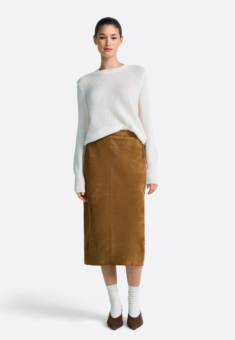 Beli pleteni pulover z dolgimi rokavi, kombiniran z rjavo semiš krilo do sredine tele. Model nosi krem nogavice in rjave koničaste pete.