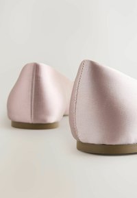 Vaaleanpunaiset satiininetoflatit, joiden kärki on terävä ja pinta sileä. Niissä on matala ruskea pohja ja ommeltuja yksityiskohtia kantapäässä.