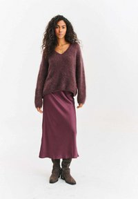 Bordowy sweter z mieszanki wełny z dekoltem w serek i długimi rękawami, zestawiony z satynową bordową suknią maxi i brązowymi zamszowymi kozakami za kolano.