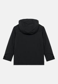 Jachetă impermeabilă neagră, cu glugă, mâneci lungi și accente cu velcro la manșete. Textură netedă, cu un design minimalist.